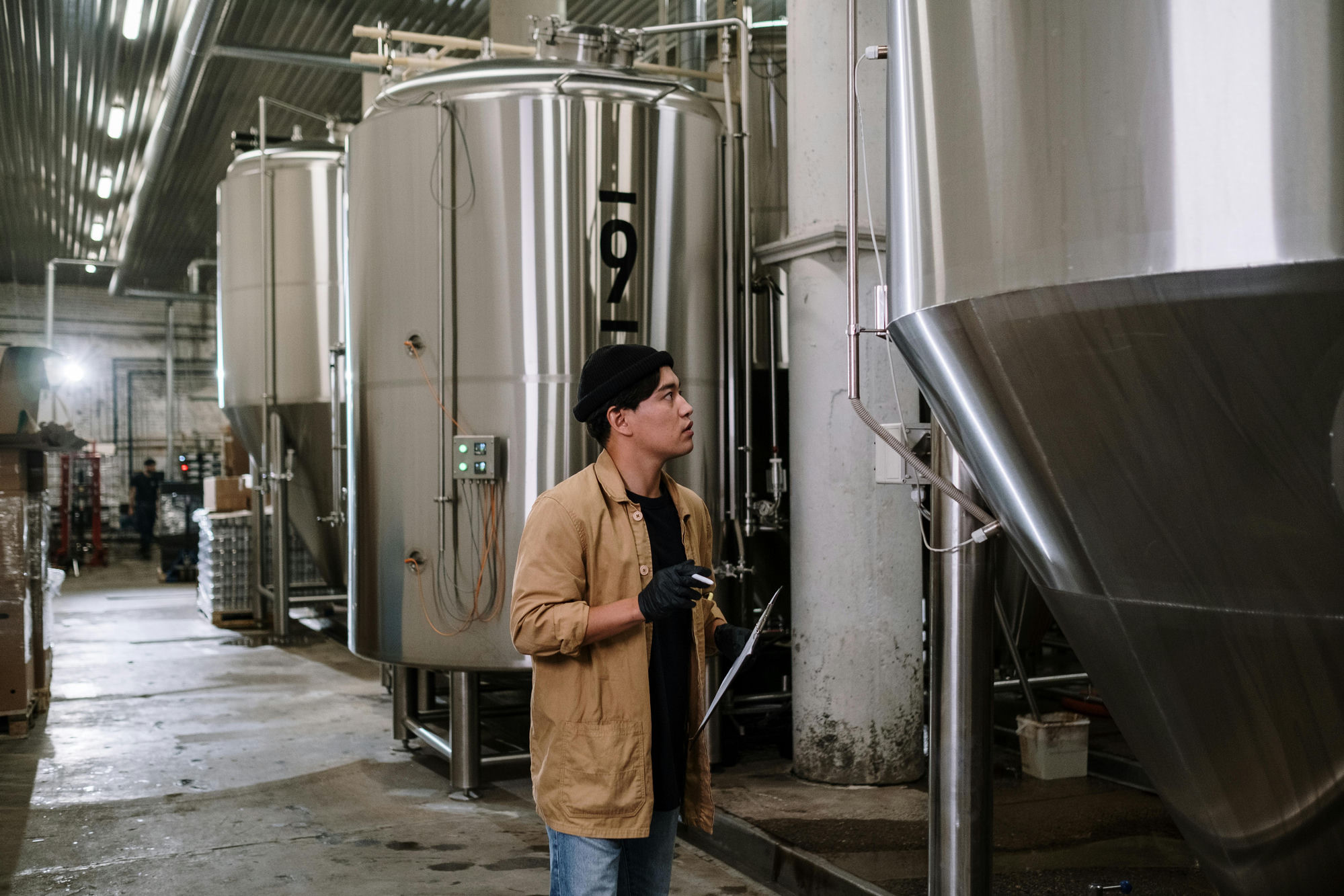 QA inspector with clipboard at stainless-steel brewing tanks